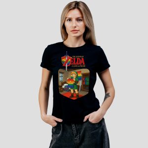 Une femme portant un T-shirt noir avec des illustrations LGBTQIA+ colorées de The Legend of Zelda : A Link to Pride, avec Link tenant un drapeau arc-en-ciel, se tient à l'intérieur d'une pièce sur un fond gris uni.