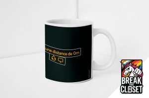 Un mug blanc avec un panneau noir comportant une bulle de texte jaune indiquant "une distance de 0m", des icônes de feu et de chat. Dans le coin, un autocollant représentant une licorne avec un drapeau arc-en-ciel et BREAK THE CLOSET, célébrant la fierté LGBTQIA+.