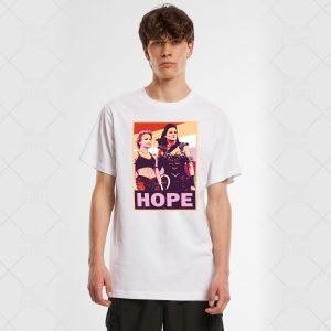 Un jeune homme portant un T-shirt blanc avec une image de style pop art de deux femmes homosexuelles avec le mot HOPE en lettres grasses au-dessous d'elles. L'arrière-plan est clair et l'homme regarde la caméra.
