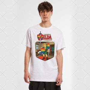 Un jeune homme portant un T-shirt blanc avec un graphique coloré de The Legend of Zelda : A Link to Pride avec Link tenant un drapeau arc-en-ciel célèbre la fierté queer à l'intérieur d'une pièce au fond clair et uni.