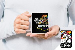 Une personne vêtue d'un pull léger tient une tasse sur laquelle figurent un T-Rex aux couleurs de l'arc-en-ciel, le texte Bitch, I'm the Queen Rarr ! et Jurassic Pride (fierté jurassique). Dans le coin, un logo "Break the Closet" avec une licorne arc-en-ciel célèbre la fierté LGBTQIA+.