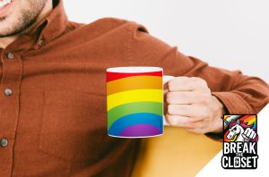 Une personne souriante, vêtue d'une chemise brune, tient une tasse avec un motif arc-en-ciel, célébrant la fierté LGBT. Dans le coin inférieur droit, le logo "Break the Closet" représente une licorne sur fond d'arc-en-ciel.