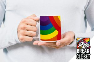 Une personne vêtue d'une chemise claire tient une tasse avec un motif arc-en-ciel, célébrant la fierté LGBTQIA+. Dans le coin inférieur droit, on trouve le logo d'un poing de licorne et le texte "BREAK THE CLOSET".