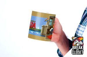 Une personne vêtue d'une chemise à carreaux tient une tasse représentant un château avec un drapeau arc-en-ciel et le texte The Legend of Zelda avec PRIDE en dessous, célébrant l'identité LGBTQIA+. Le logo de la licorne Break the Closet apparaît dans le coin inférieur droit.