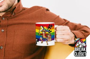 Une personne vêtue d'une chemise brune tient une tasse avec des personnages d'anime, sur fond de drapeau de la fierté arc-en-ciel et d'un logo LGBT "Break the Closet" représentant une licorne et un drapeau arc-en-ciel dans le coin inférieur droit.