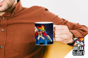 Une personne vêtue d'une chemise brune tient un mug représentant un robot coloré aux accents arc-en-ciel. Dans le coin, un logo "Break the Closet" avec une licorne arc-en-ciel et un texte en gras célèbre la fierté LGBT.