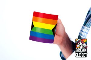 Une personne portant une chemise à carreaux tient un mug dont les rayures arc-en-ciel et noires rappellent le drapeau de la fierté. Dans le coin, un logo de licorne "Break the Closet" aux couleurs de l'arc-en-ciel célèbre la fierté LGBTQIA+.