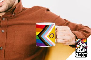 Une personne vêtue d'une chemise de couleur rouille tient un mug sur lequel figure le drapeau de la fierté LGBTQIA+ Progress avec une inclusion intersexe. Dans le coin, un logo "Break the Closet" avec une licorne et les couleurs de l'arc-en-ciel célèbre la visibilité des homosexuels.