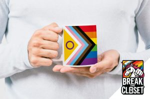 Une personne vêtue d'un pull léger tient un mug sur lequel figurent le drapeau Progress Pride et le drapeau intersexe, célébrant la fierté LGBTQIA+. En bas à droite, on peut voir le logo "Break the Closet" avec une licorne et les couleurs de l'arc-en-ciel.