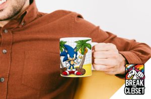 Une personne vêtue d'une chemise brune tient un mug à l'effigie de Sonic le hérisson, entouré de palmiers. Dans le coin, un logo coloré "Break the Closet" avec une licorne et un arc-en-ciel célèbre la fierté LGBTQIA+.
