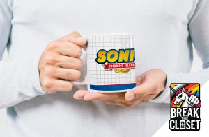 Une personne en chemise blanche tient une tasse avec un graphique SONI COCKRING ISLAND imitant le logo de Sonic the Hedgehog. Dans le coin inférieur droit, un logo "Break the Closet" avec une licorne arc-en-ciel souligne la fierté homosexuelle.