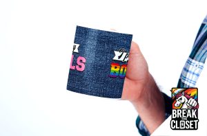 Une personne vêtue d'une chemise à carreaux tient un mug bleu à motif denim avec un texte coloré, dont "BOYS" dans les couleurs de l'arc-en-ciel. Un logo de licorne avec "BREAK THE CLOSET" apparaît en bas à droite, célébrant la fierté queer et LGBTQIA+.