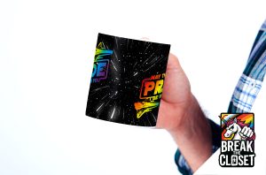 Une personne tient une tasse avec un arrière-plan sur le thème de l'espace et un texte coloré qui dit May the Pride Be With You (Que la fierté soit avec vous). Dans le coin, un logo "Break the Closet" avec une licorne et des couleurs arc-en-ciel célèbre la fierté LGBTQIA+.