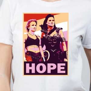 Une personne porte un tee-shirt avec une illustration colorée et stylisée de deux femmes guerriÚres queer se tenant cÎte à cÎte, avec le mot HOPE en lettres roses en gras au-dessous d'elles.