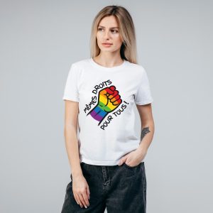 Une femme se tient sur un fond gris uni, vêtue d'un t-shirt blanc avec un poing fermé aux couleurs de l'arc-en-ciel et le texte français "Mêmes droits pour tous" - une déclaration audacieuse en faveur de l'égalité des droits pour les personnes LGBTQIA+.