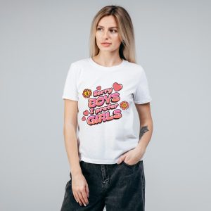 Une femme aux longs cheveux blonds portant un T-shirt blanc sur lequel on peut lire Sorry boys, I prefer girls en lettres colorées et ludiques avec des fleurs et des cœurs, debout sur un fond gris uni - affichant fièrement son style queer.
