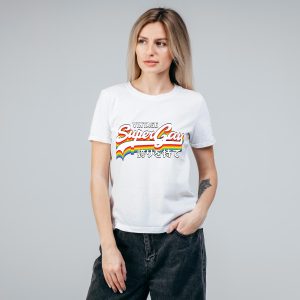 Une personne portant un t-shirt blanc avec un arc-en-ciel coloré et le texte Vintage Super Gay en caractères japonais se tient sur un fond gris uni, exprimant fièrement son identité queer.