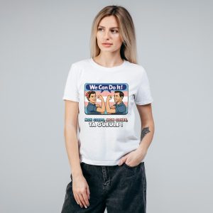 Une femme aux longs cheveux blonds porte un t-shirt blanc représentant une caricature de deux femmes en train de s'assouplir, We Can Do It ! au-dessus d'elles, et Mon corps, mon genre, ta gueule ! en dessous, célébrant la fierté queer sur un fond gris uni.