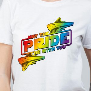 Une personne porte un T-shirt blanc avec des vaisseaux spatiaux aux couleurs de l'arc-en-ciel et un texte en gras indiquant "May the PRIDE be with you", célébrant la fierté LGBTQIA+ avec un thème de science-fiction parfait pour les communautés queer.