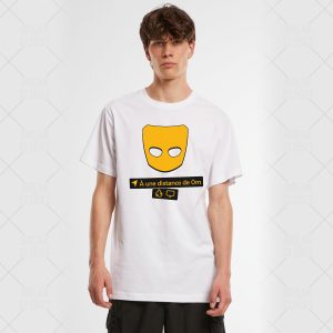 Un jeune homme aux cheveux bruns courts porte un T-shirt blanc sur lequel figurent un masque jaune, le texte français "À une distance de 0m", une petite bulle de dialogue et des symboles de caméra - célébrant subtilement la fierté LGBTQIA+ sur un fond clair et uni.