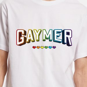 Un T-shirt blanc portant le mot GAYMER en caractères gras et arc-en-ciel, avec six cœurs arc-en-ciel en dessous - un fier clin d'œil à la communauté des joueurs queers et LGBT.