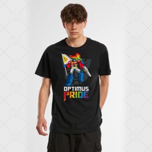 Un jeune homme portant un t-shirt noir avec un robot coloré tenant un drapeau arc-en-ciel et les mots OPTIMUS PRIDE en lettres grasses aux couleurs de l'arc-en-ciel célèbre la fierté LGBT.