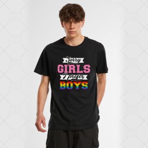Une personne aux cheveux bruns courts porte un T-shirt noir avec le texte Sorry girls, I prefer boys en lettres roses, blanches et arc-en-ciel - une déclaration audacieuse de fierté LGBT. L'arrière-plan est blanc.