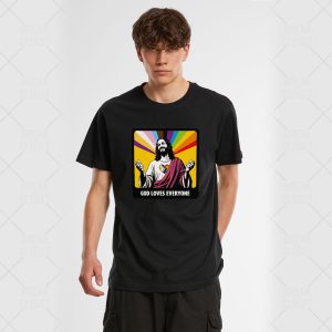 Un jeune homme portant un t-shirt noir avec une illustration de Jésus avec des rayons arc-en-ciel en arrière-plan et le texte God Loves Everyone (Dieu aime tout le monde), célébrant la fierté LGBTQIA+.