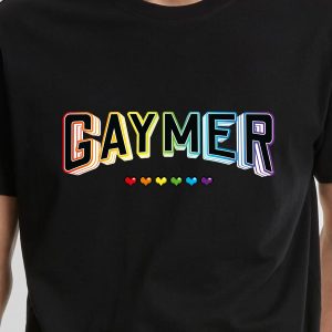 Une personne portant une chemise noire avec le mot GAYMER en lettres 3D de couleur arc-en-ciel et six petits cœurs de couleur arc-en-ciel en dessous, célébrant fièrement l'identité queer et LGBTQIA+.