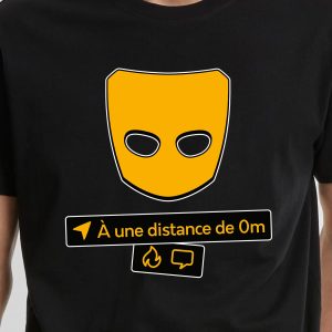 Une personne portant une chemise noire avec un masque jaune au-dessus d'un texte en français indiquant À une distance de 0m, ainsi que des icônes pour la localisation, la flamme et le chat - un clin d'œil subtil aux communautés queer et LGBTQIA+.