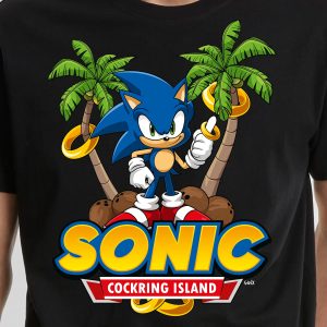 Un t-shirt montre Sonic le hérisson debout parmi des palmiers et des noix de coco, tenant des anneaux d'or. En dessous, on peut lire SONIC et COCKRING ISLAND en caractères gras et colorés, un clin d'œil amusant à la fierté queer et LGBTQIA+.